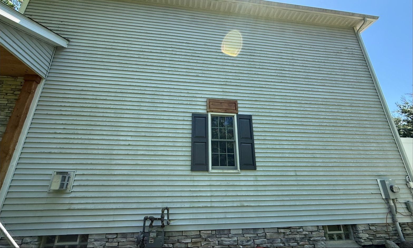 Before, vinyl siding covered in algae streaking around a window